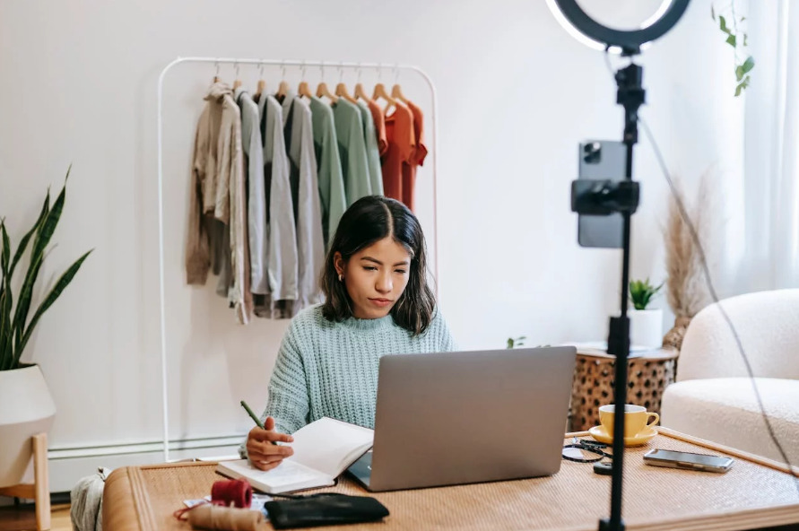 Une femme assise à un bureau, utilisant un ordinateur portable et une caméra.