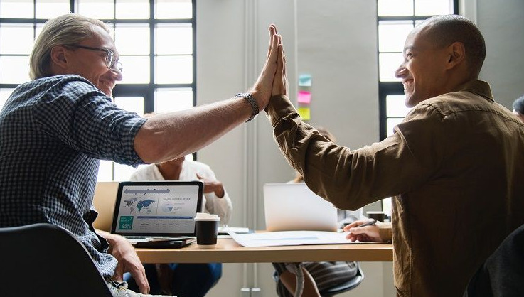 Deux hommes se donnent un high five dans un bureau, exprimant la camaraderie et la réussite professionnelle.